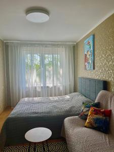 a bedroom with a bed and a couch and a window at LINA apartment with balcony in Klaipėda