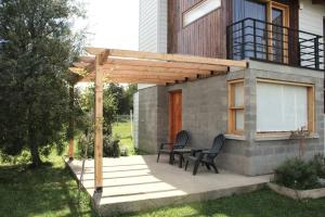a patio with two chairs and a wooden pergola at Origen Rent a house in El Bolsón