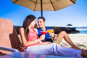 a man and woman sitting under an umbrella on the beach at Estero Beach Hotel & Resort in Ensenada