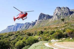 a red helicopter is flying over a mountain at Twelve Apostles Hotel & Spa in Cape Town