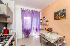 a kitchen with purple curtains and a table with flowers at Appartamento posizione comoda in Collegno