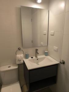 Un baño con lavabo, inodoro y espejo. en Departamento nuevo en Rondizzoni, en Santiago
