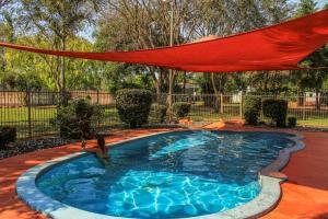 a swimming pool with a red umbrella over it at Banyan Tree Holiday Park in Rum Jungle Station