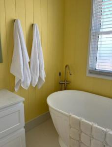 a white bath tub in a yellow bathroom with towels at Daffodil on Owen in Huskisson +9 photos