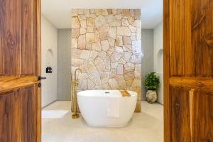 a bath tub in a bathroom with a stone wall at 3min walk to the beach, night market, restaurant, Humble House 2 in Amphoe Koh Samui +20 photos