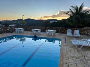 una piscina con sedie e tavoli e il tramonto di Recanto da Felicidade a São Lourenço
