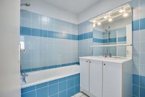 ein blau gefliestes Bad mit einem Waschbecken und einer Badewanne in der Unterkunft Résidence Odalys Le Hameau du Lac in Rignac
