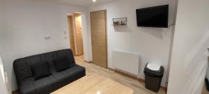 ein Wohnzimmer mit einem schwarzen Sofa und einem Flachbild-TV in der Unterkunft AU MENILOIS entre Montagne et Forêt in Cornimont