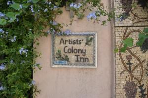 un cartello sul lato di un muro con dei fiori di Artists' Colony Inn Zefat a Safed