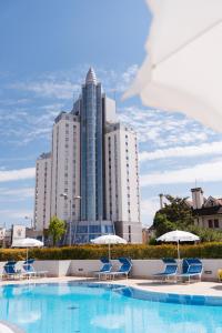 a pool with chairs and umbrellas in front of a tall building at Anima Jesolo - Drago Village - Family Apartments - City Center, Pool & Garden, Beach Umbrella Included, 2 Parking Spaces in Lido di Jesolo