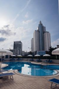 a swimming pool with chairs and umbrellas in a city at Anima Jesolo - Drago Village - Family Apartments - City Center, Pool & Garden, Beach Umbrella Included, 2 Parking Spaces in Lido di Jesolo