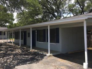 a white house with a porch with trees in the background at La Vista Motel in Burnet