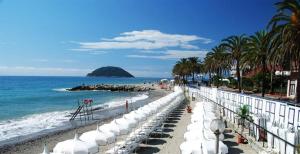 una spiaggia con ombrelloni bianchi e l'oceano di Ampio appartamento vista mare per 6 persone ad Albenga