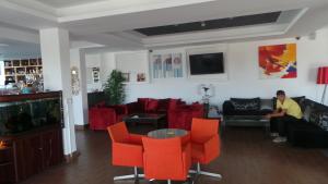 Neptune Hotel Apartments Paphos في كورال باي: غرفة معيشة مع كراسي حمراء ورجل يجلس على أريكة