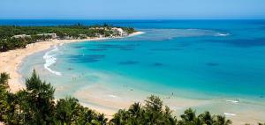 a beach with people swimming in the ocean at Seaside Apartment Steps to Breathtaking Sunrise in Luquillo