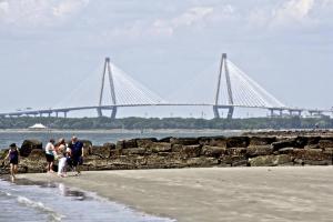 a group of people walking on the beach with a bridge in the background at Lazy Lagoon in Kiawah Island