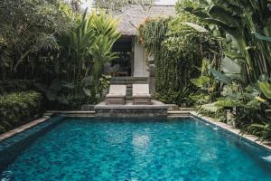 una piscina con dos sillas y una casa en Kharista Villas & Retreat by Ekosistem, en Canggu
