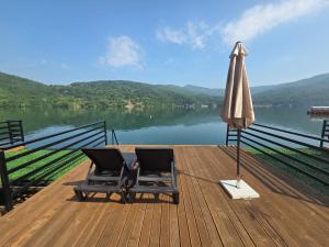 an umbrella and two chairs on a wooden deck with a lake at Villa Razlicak - Jezero Lake Perucac in Perućac