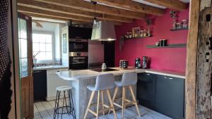 a kitchen with pink walls and a counter with stools at La petite normande in Appeville-Annebault