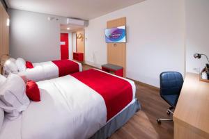 a hotel room with two beds and a chair at Ramada Encore by Wyndham Guadalajara Aeropuerto in Guadalajara