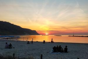 a group of people sitting on the beach watching the sunset at casa di Baia in Pesaro