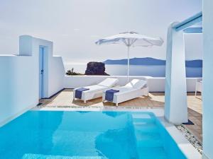 a swimming pool with an umbrella and chairs and an ocean at Astra Suites in Imerovigli