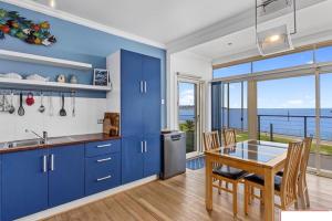 una cocina con armarios azules y una mesa con vistas al océano. en crystal blue apartment, en Port Vincent