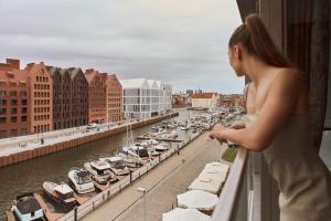 a woman standing on a balcony looking at a marina at Waterlane Riverside SPA, Pool & Gym by Downtown Apartments in Gdańsk +42 photos