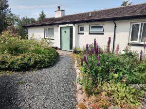 a white house with a green door and some flowers at Cartmel in Aultbea