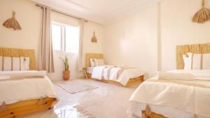 a white room with two beds and a window at Sable Beach Surf Camp & Hostel Tamraght in Tamraght Ouzdar