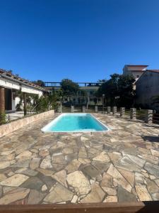 a swimming pool with a stone patio and blue sky at Pousada Vale Do Aijalom in Cabo Frio