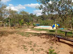 eine Bank mit einem Regenschirm neben einem Pool in der Unterkunft Camping dos oliveira in Jaboticatubas