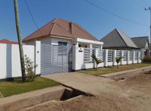 ein weißes Haus mit einem Zaun und einigen Bäumen in der Unterkunft Beskydy Holiday Rentals in Mbeya
