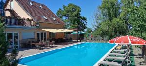 a swimming pool with a red umbrella and chairs at Tabán Vendégház in Balatonlelle