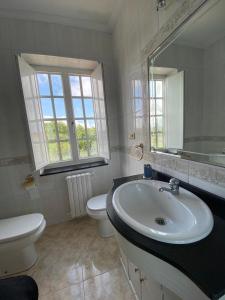 ein Badezimmer mit Waschbecken, Toilette und Spiegel in der Unterkunft Casa con encanto amplios jardines al lado de la playa in Caleiro