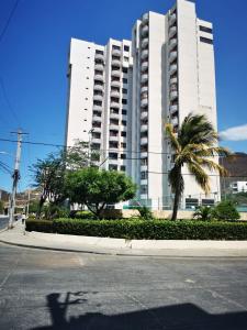 a large white building with palm trees in front of it at Apartamento en condominio con piscina, cerca a la playa El Rodadero in Gaira