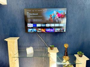 une télévision suspendue sur un mur avec une table en verre dans l'établissement Casa Espaçosa 6 Qts Churrasqueira 10 min Praia do Forte, à Cabo Frio