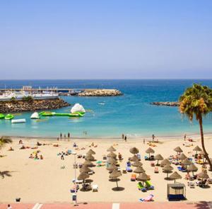 a beach with people and umbrellas and the ocean at Gran View Apartment Sea Wiew, WiFi,Garage, Car rental in Adeje