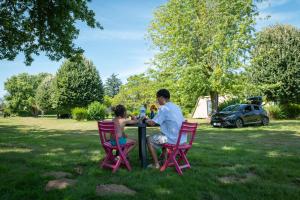 a man and woman sitting at a table in a park at Camping Onlycamp La Potinière in Écueillé