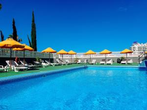 a swimming pool with umbrellas and chairs and a building at Olympia Palmalicious Apartment in Playa de las Americas
