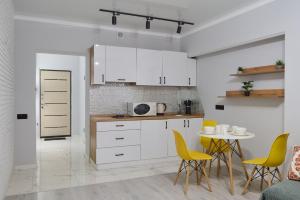 One Bedroom Apartment Next to Arbat In The Center of Almaty في ألماتي: مطبخ مع دواليب بيضاء وطاولة مع كراسي صفراء