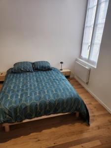a bedroom with a bed with a blue comforter and two windows at Appartement 103 in Avallon