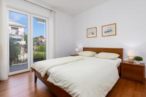 a white bedroom with a bed and a large window at Apartments Bogović in Malinska