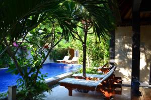 a resort pool with two lounge chairs and palm trees at Taman Senang in Gili Air