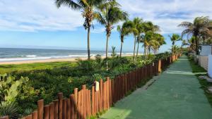 a wooden fence next to a beach with palm trees at Refúgio Guarajuba, 50m da Praia, Piscina, Recarga EV, área gourmet, churrasqueira in Camaçari
