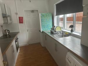 a kitchen with white cabinets and a sink and a window at Cosy 4 Bedroom Walsall House - Free WiFi & Parking in Bescot