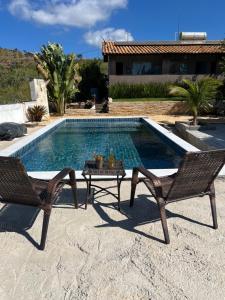 a swimming pool with two chairs and a table next to it at Pousada Sabia Capitolio in Capitólio