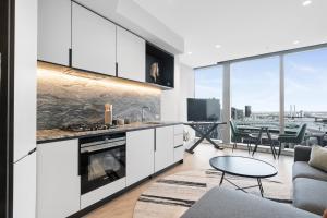 eine Küche mit weißen Schränken und ein Wohnzimmer mit einem Tisch in der Unterkunft West Side Spencer St Apt w Marvel Stadium View in Melbourne