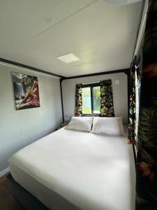 een groot wit bed in een kleine kamer met een raam bij Nui Stay in Haapiti