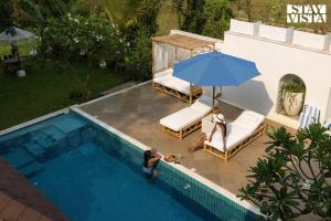 two people sitting under an umbrella next to a swimming pool at StayVista at Villa Selene - Dolly J Homes with Pool in Sangolda